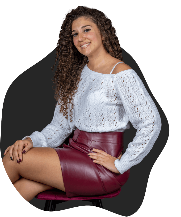 Jessica seduta su una sedia, con maglione chiaro e gonna bordeaux, ritratta in uno scatto professionale